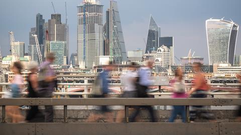 Blurred passers-by walk in front of the London City skyline