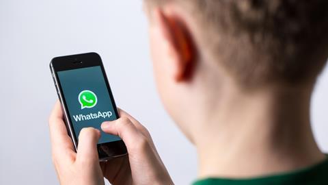 A boy holds a phone that displays the Whatsapp logo