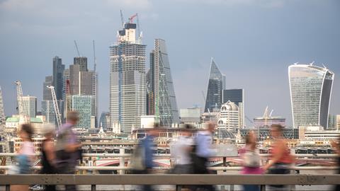 Blurred passers-by walk in front of the London City skyline