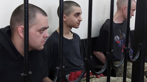 Two British citizens Aiden Aslin, left, and Shaun Pinner, right, and Moroccan Saaudun Brahim, center, sit behind bars in a courtroom in Donetsk