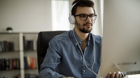A male office worker wears headphones while typing at his desk