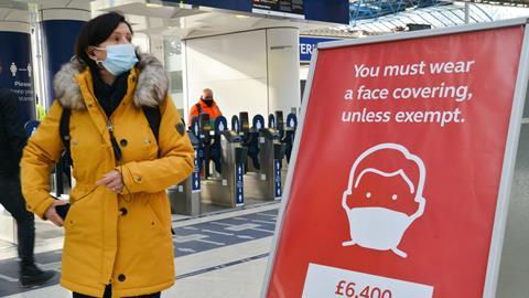 A commuter wearing a face mask walks past a sign at London Waterloo train station reminding the public they can be fined for not wearing one