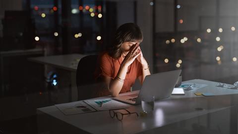 A woman sits at her office desk late at night with her head in her hands