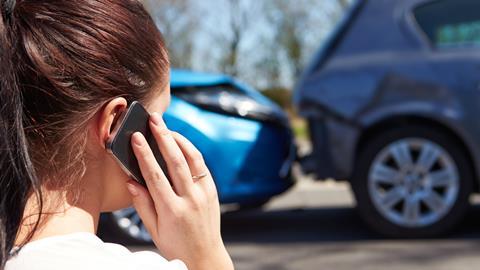 A woman speaks on the phone as she looks at the damage to her car after a crash