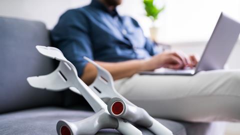 Crutches lay on a sofa next to a blurred image of a man on a laptop