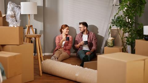 A couple sit on the floor of their new home surrounded by boxes