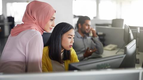 A young office worker helps out a colleague at a computer