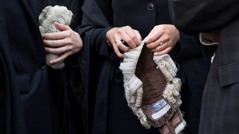 Barristers wearing gowns hold their wigs in their hands