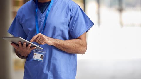An anonymous doctor in hospital scrubs checks a tablet