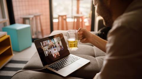 Man holds up glass of beer in front of laptop while video-calling colleagues