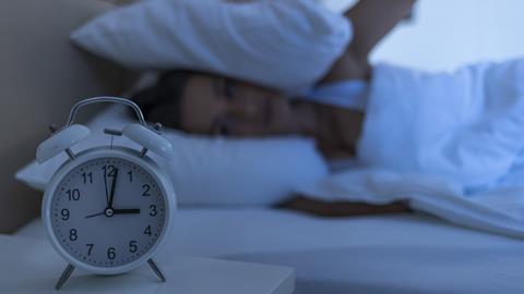 A woman lay in bed stares at her alarm clock showing 3 a.m
