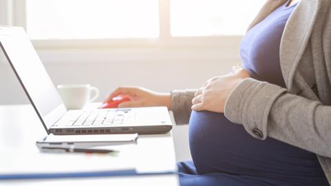 A pregnant woman rests her hand on her baby bump as she works at a laptop