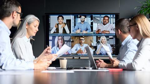 A group of four colleagues sit round a table while listening to clients on a virtual call