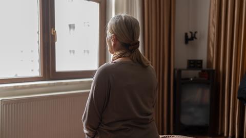 An older woman looks out of her bedroom window
