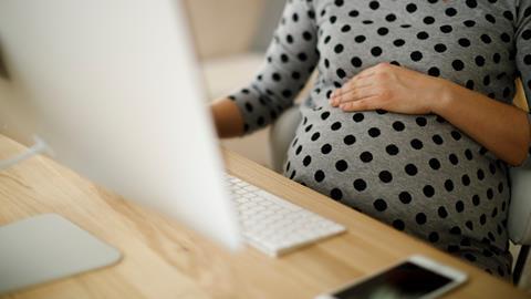 A pregnant woman rests her hand on her bump as she works on her computer