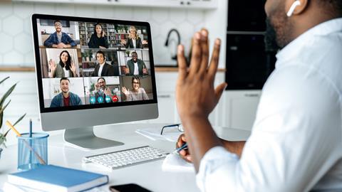 A man waves to his colleagues on a video call while working from home