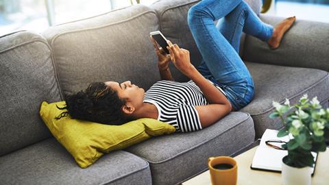 A woman lies on the sofa scrolling on her phone