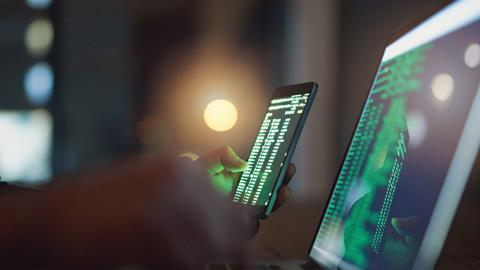Hacker holds phone showing coding