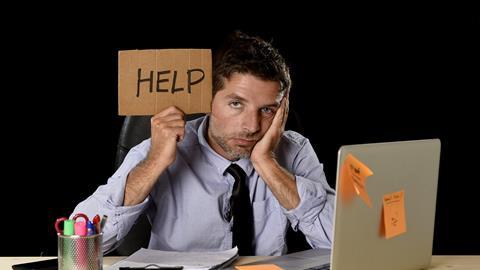 Exasperated man holding up a sign reading 'Help' as he sits in front of a laptop
