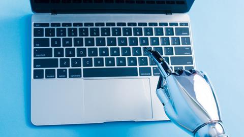 A robot hand types on a laptop keyboard