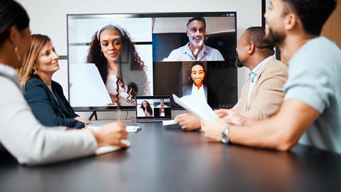 Four colleagues in an office meeting room chat to coworkers on screen