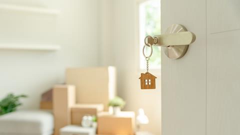 A house keyring hangs from a key in a lock, showing moving boxes behind the open door