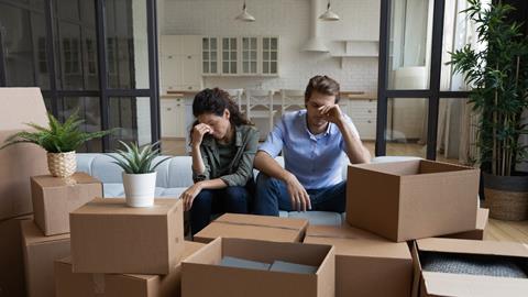 A young couple sit with their heads in their hands surrounded by moving boxes