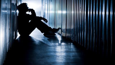 The silhoutte of a young man sits on the floor of a cell