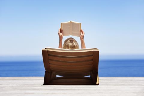 Sunbather reads book on lounger overlooking the sea