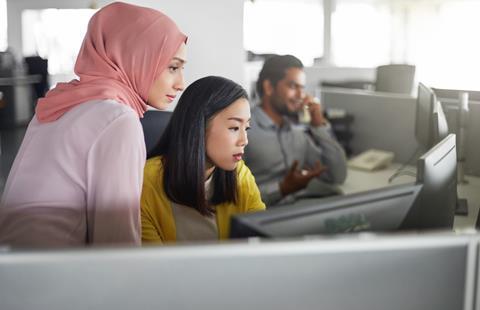 A young office worker helps out a colleague at a computer