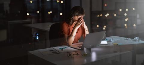 A woman sits at her office desk late at night with her head in her hands