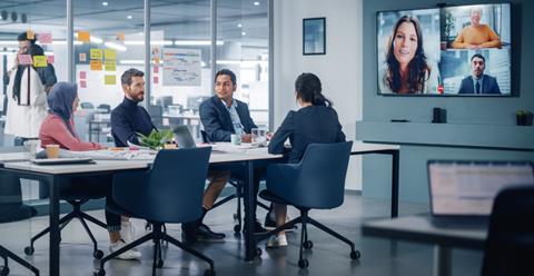 Collegues chat in an office meeting room while others appear on screen