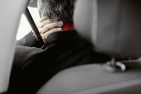 A man in a car holds his neck in pain