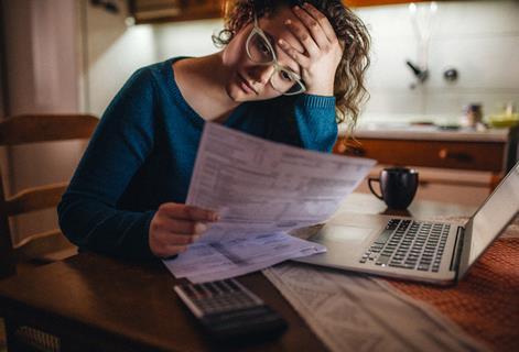 A woman reads a bill with her head in her hands