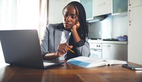 A female student sits in front of a laptop with a book open on the desk