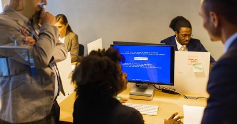 Colleagues gather round a co-worker's computer screen that displays a system error page