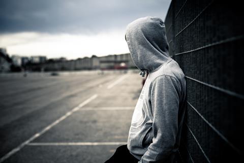 An anoymous teenager wearing a hoody leans on a fence