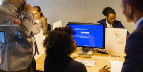 Colleagues gather round a co-worker's computer screen that displays a system error page