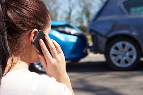 A woman speaks on the phone as she looks at the damage to her car after a crash