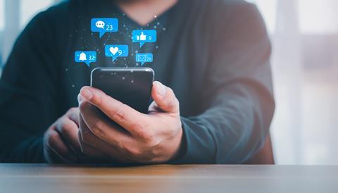 A man looks at his phone with various social media graphics appearing above the screen