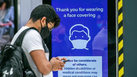 A traveler wearing mask at Waterloo station stands in front of a Covid safety sign