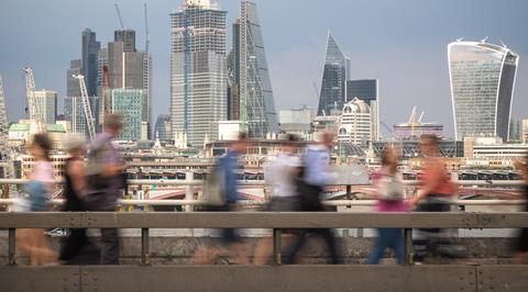 Blurred passers-by walk in front of the London City skyline