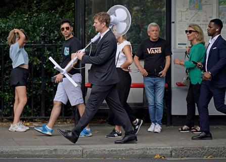 A man wearing a suit carries a large fan over his shoulder through Westminster