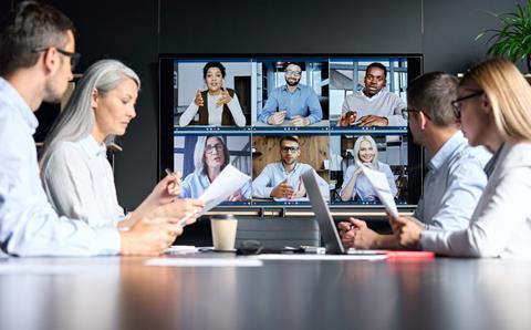 A group of four colleagues sit round a table while listening to clients on a virtual call