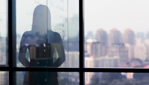 A silhouette of a woman against the backdrop of a window overlooking a city skyline