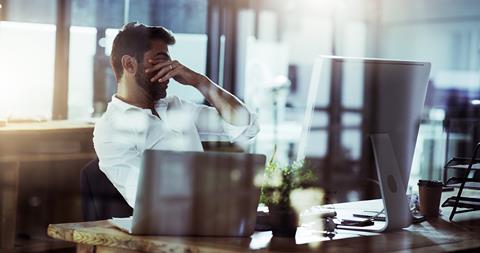 A tired man puts his hands over his eyes while sat at his desk