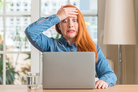A young woman holds a hand to her forehead as she looks worried at her laptop