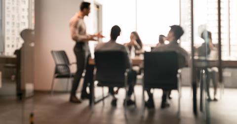 A blurred image of a team meeting taking place at the office