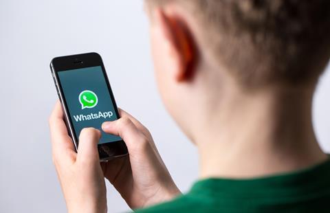A boy holds a phone that displays the Whatsapp logo