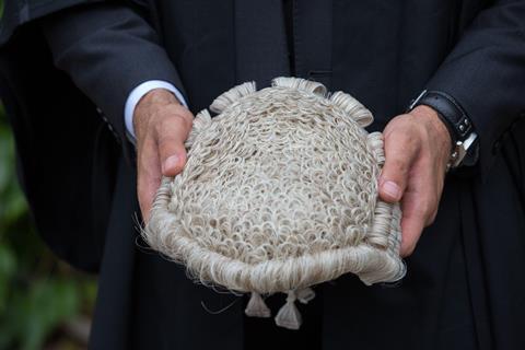 An anonymous man holds a barrister wig